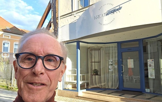 Pop-up-Store informiert über Katholikentag Ein älterer Mann mit Brille und rotem Pullover steht vor einem Geschäft. Das Geschäft hat ein Schild mit der Aufschrift